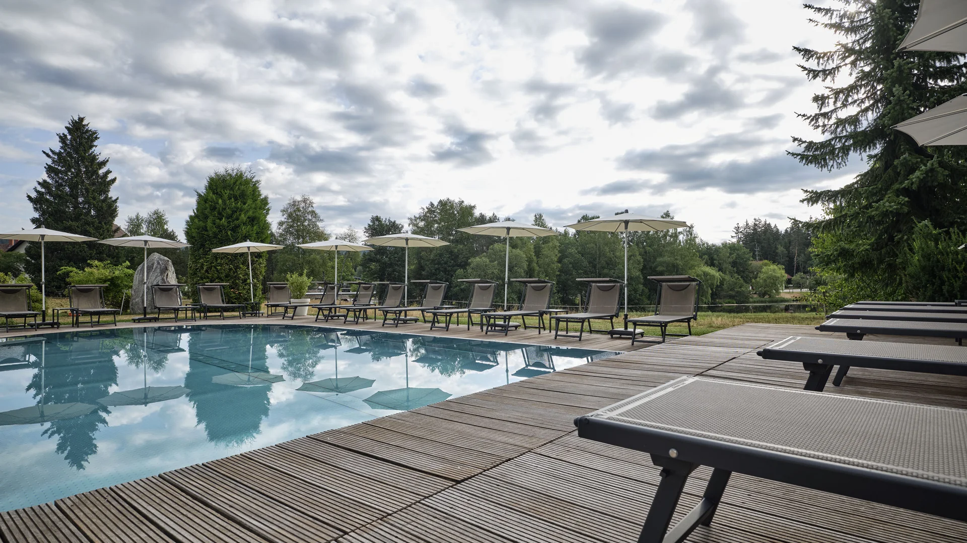 Leerer Swimmingpool mit Liegestühlen und Sonnenschirmen bei bewölktem Himmel