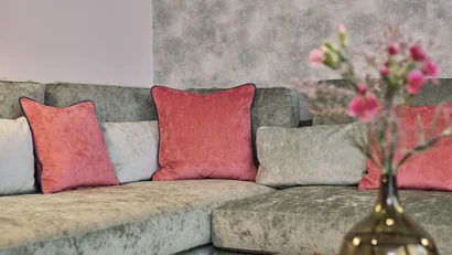 Gemütliche graue Couch mit roten und grauen Kissen und Vase mit Blumen