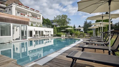 Poolbereich mit Liegestühlen und Sonnenschirmen neben einem Hotelgebäude