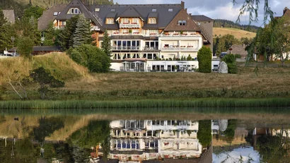 Hotelgebäude mit Dachgauben und Blumen, vom See im Vordergrund gespiegelt