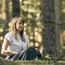 Frau meditiert entspannt im Wald sitzend mit geschlossenen Augen