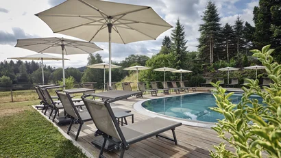 Leere Liegestühle mit Sonnenschirmen neben einem Pool in einer bewaldeten Landschaft