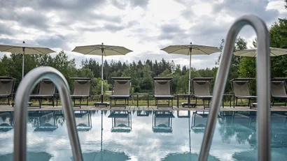 Pool mit Sonnenliegen und Schirmen vor bewölktem Himmel und Wald