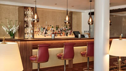Eleganter Hotelbarbereich mit Holz, roten Barhockern und beleuchteten Regalen