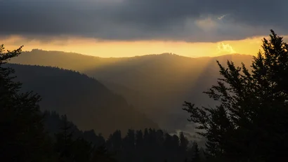 Sonnenstrahlen durch Wolken über bewaldeten Bergen bei Sonnenuntergang