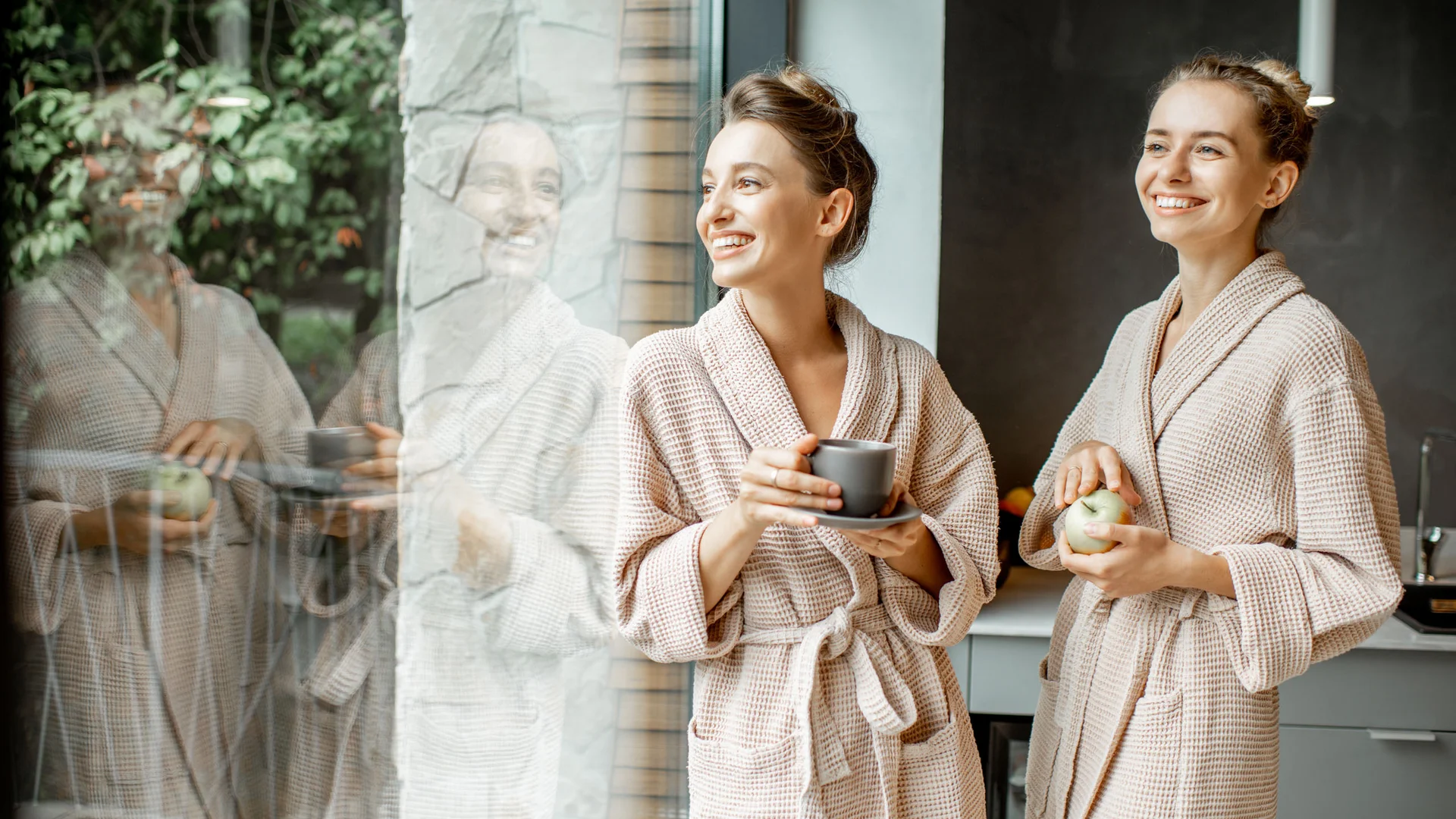 Zwei Frauen in Bademänteln trinken Kaffee und essen Apfel in der Küche